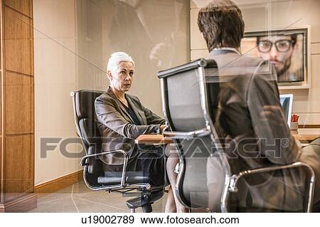 View through glass of businesspeople sitting on office chairs making video call View Large Photo Image Stock Photo - View through glass of businesspeople sitting on office chairs making video call. Fotosearch
