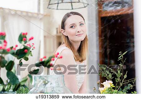 Stock Photo - View through glass of flowers and woman looking away. Fotosearch