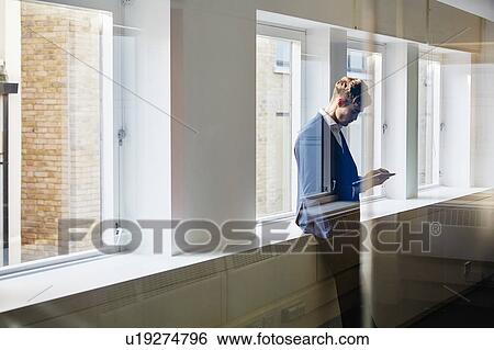 View through glass of man leaning against windowsill looking down at smartphone View Large Photo Image Stock Photograph - View through glass of man leaning against windowsill looking down at smartphone. Fotosearch