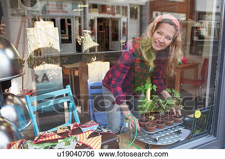 Stock Photograph - View through glass of woman arranging window display. Fotosearch