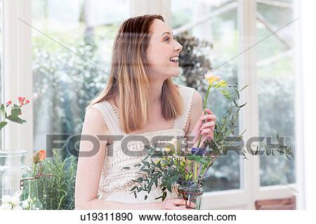 Stock Image - View through glass of woman holding flower looking away smiling. Fotosearch