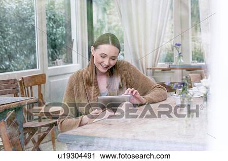 View through glass of woman sitting at table using digital tablet smiling View Large Photo Image Stock Image - View through glass of woman sitting at table using digital tablet smiling. Fotosearch