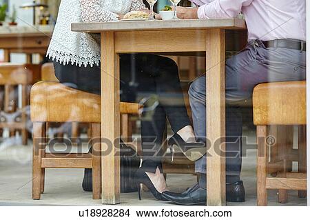 Picture - Waist down view of womans high heel shoe touching mans leg at restaurant table. Fotosearch