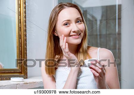 Stock Photo - Woman applying face cream looking at camera smiling. Fotosearch