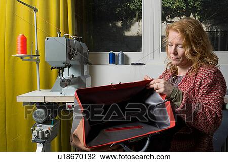 Stock Image - Woman at sewing machine assembling leather holdall. Fotosearch