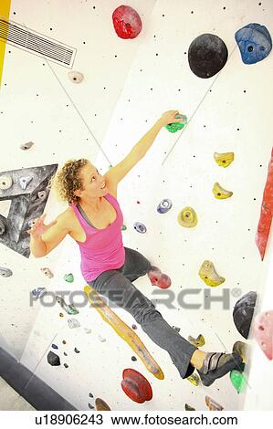 Stock Image - Woman climbing indoor artificial climbing wall. Fotosearch