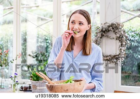 Stock Photography - Woman eating salad leaves looking away. Fotosearch