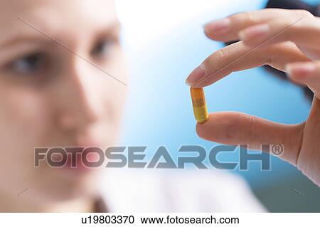 Stock Image - Woman holding a capsule, close up. Fotosearch