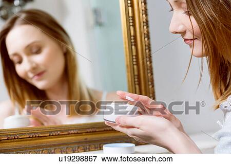 Stock Photo - Woman holding face cream looking down smiling. Fotosearch