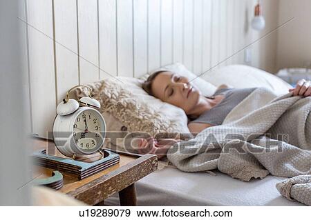 Stock Photo - Woman in bed, alarm clock on bedside table. Fotosearch