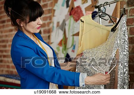 Stock Photo - Woman in design studio looking at garments. Fotosearch