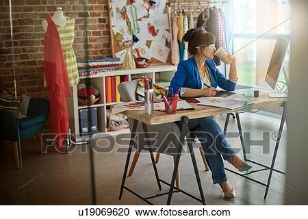 Stock Image - Woman in design studio sitting at desk looking away. Fotosearch