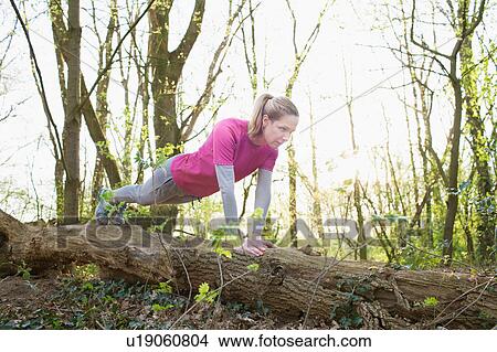 Picture - Woman in forest doing press ups on fallen tree. Fotosearch