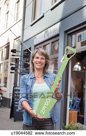 Woman in front of shop holding open sign looking at camera smiling View Large Photo Image Stock Image - Woman in front of shop holding open sign looking at camera smiling. Fotosearch