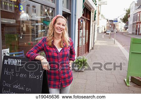 Woman in front of shop leaning against a-frame looking at camera smiling View Large Photo Image Stock Photograph - Woman in front of shop leaning against a-frame looking at camera smiling. Fotosearch