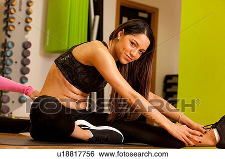 Woman in gym sitting on floor doing leg stretching exercises looking at camera smiling View Large Photo Image Stock Photograph - Woman in gym sitting on floor doing leg stretching exercises looking at camera smiling. Fotosearch