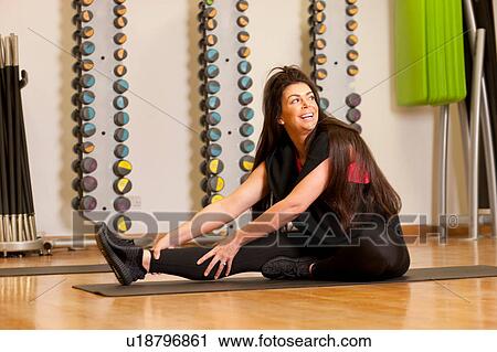 Woman in gym sitting on yoga mat stretching legs View Large Photo Image Stock Image - Woman in gym sitting on yoga mat stretching legs. Fotosearch