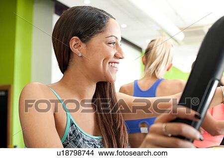 Woman in gym using exercise equipment looking away smiling View Large Photo Image Picture - Woman in gym using exercise equipment looking away smiling. Fotosearch