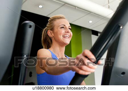 Stock Image - Woman in gym using exercise machine smiling. Fotosearch
