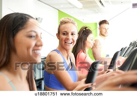 Stock Image - Woman in gym using exercise machine smiling. Fotosearch