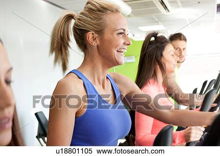 Stock Photography - Woman in gym using exercise machine smiling. Fotosearch
