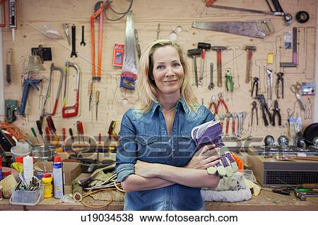 Woman in workshop, arms crossed holding protective gloves looking at camera smiling View Large Photo Image Stock Photo - Woman in workshop, arms crossed holding protective gloves looking at camera smiling. Fotosearch