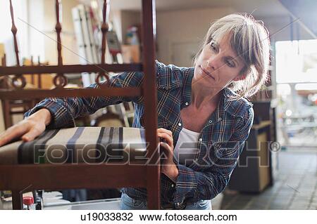 Stock Image - Woman in workshop examining chair. Fotosearch
