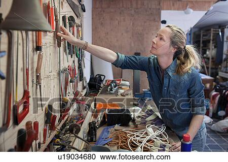Woman in workshop reaching for tools hung on wall View Large Photo Image Stock Image - Woman in workshop reaching for tools hung on wall. Fotosearch