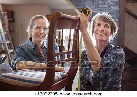 Stock Photography - Woman in workshop with chair looking at camera smiling. Fotosearch
