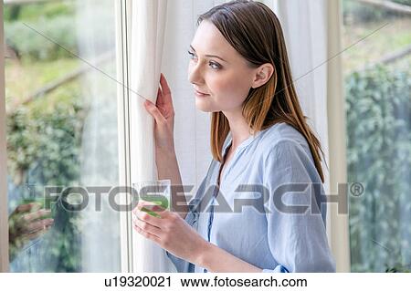 Woman looking out of window holding green smoothie View Large Photo Image Stock Image - Woman looking out of window holding green smoothie. Fotosearch