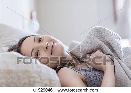 Woman lying in bed looking at camera smiling View Large Photo Image Stock Image - Woman lying in bed looking at camera smiling. Fotosearch