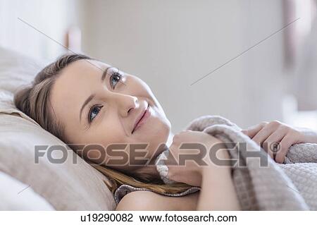 Woman lying in bed looking away smiling View Large Photo Image Stock Image - Woman lying in bed looking away smiling. Fotosearch