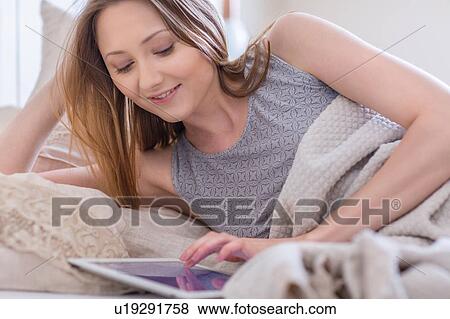Woman lying in bed using digital tablet smiling View Large Photo Image Stock Photo - Woman lying in bed using digital tablet smiling. Fotosearch