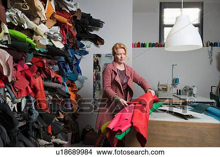Picture - Woman making selection from stack of leather skins. Fotosearch