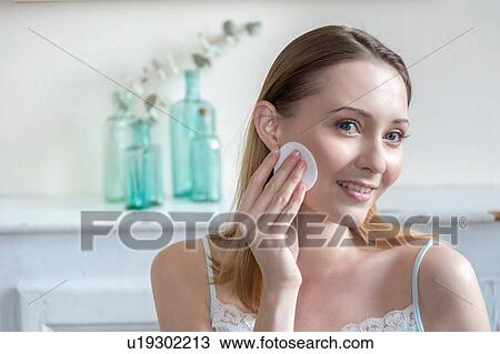 Stock Image - Woman moisturising face with cotton wool pad. Fotosearch