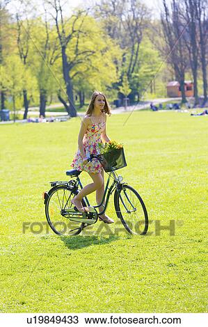 Stock Image - Woman on bicycle with flowers in basket. Fotosearch
