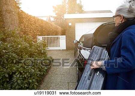 Woman on driveway in front of open car boot holding suitcase View Large Photo Image Stock Image - Woman on driveway in front of open car boot holding suitcase. Fotosearch