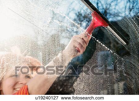 Stock Photo - Woman outdoors cleaning sunlit window with squeegee. Fotosearch