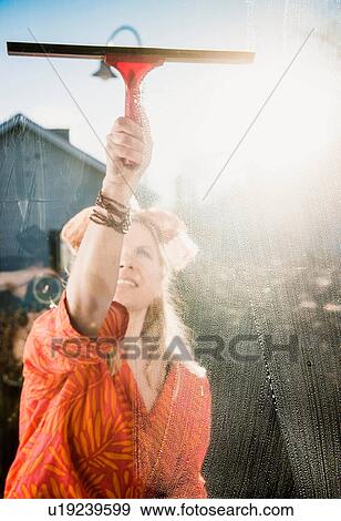 Stock Photo - Woman outdoors reaching to clean sunlit window with squeegee. Fotosearch