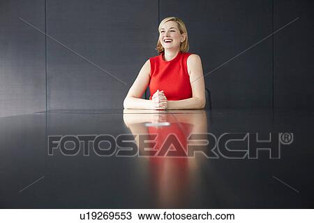 Stock Image - Woman sitting at desk hands together smiling. Fotosearch