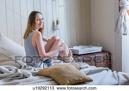 Stock Image - Woman sitting on bed looking over shoulder at camera smiling. Fotosearch