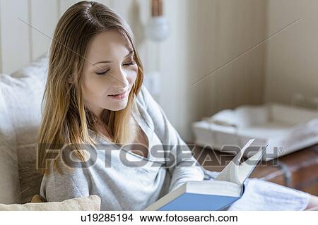 Picture - Woman sitting on bed reading book. Fotosearch