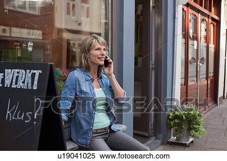 Stock Photography - Woman sitting on shop windowsill making telephone call. Fotosearch