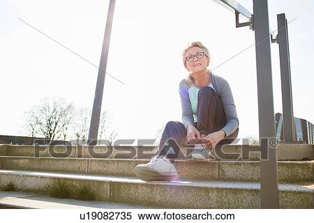 Woman sitting on steps tying shoelace looking away View Large Photo Image Stock Photography - Woman sitting on steps tying shoelace looking away. Fotosearch
