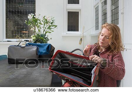 Stock Photograph - Woman sitting quality checking leather holdalls. Fotosearch