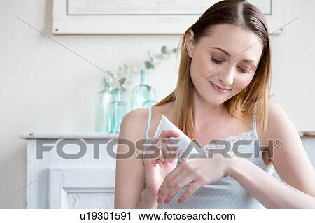 Stock Image - Woman squeezing cosmetic cream onto hand, looking down smiling. Fotosearch