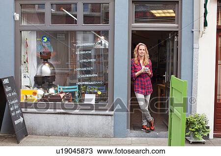 Woman standing in shop doorway holding coffee cup looking at camera View Large Photo Image Stock Image - Woman standing in shop doorway holding coffee cup looking at camera. Fotosearch