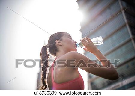 Stock Photo - Woman training, drinking bottled water in park, Dubai, United Arab Emirates. Fotosearch
