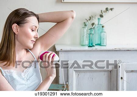 Stock Image - Woman using electric shaver to shave armpit. Fotosearch