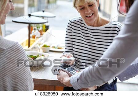Stock Image - Woman using smartphone contactless payment at restaurant table, London, UK. Fotosearch